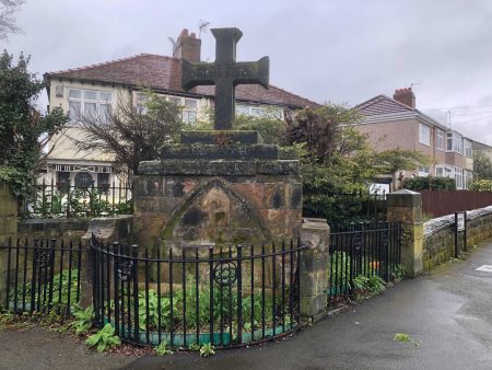 Photograph of sandstone structure topped with a stone cross and surrounded by railings.